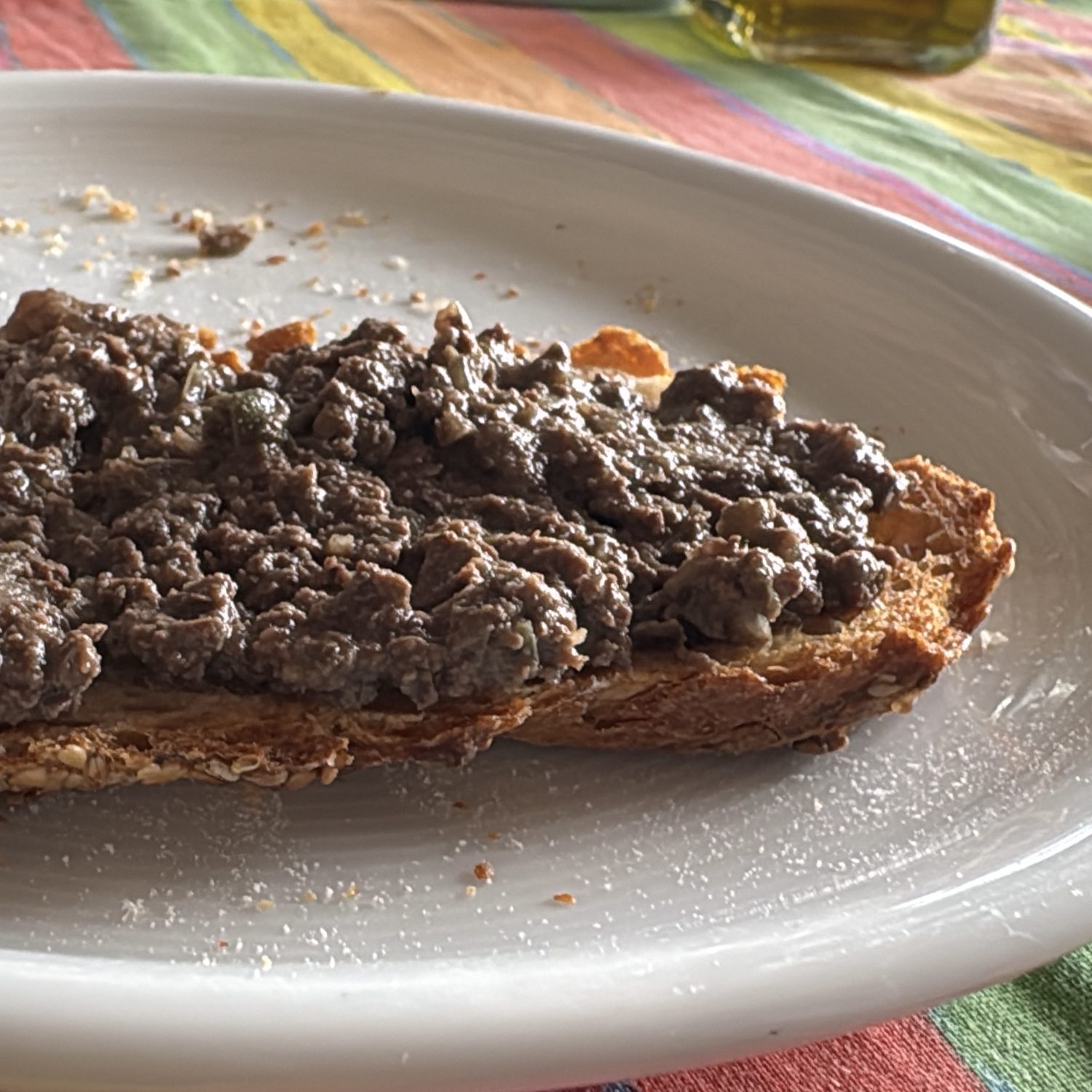 Fetta di pane tostato ricoperta di paté di fegatini scuro e granuloso su un piatto bianco